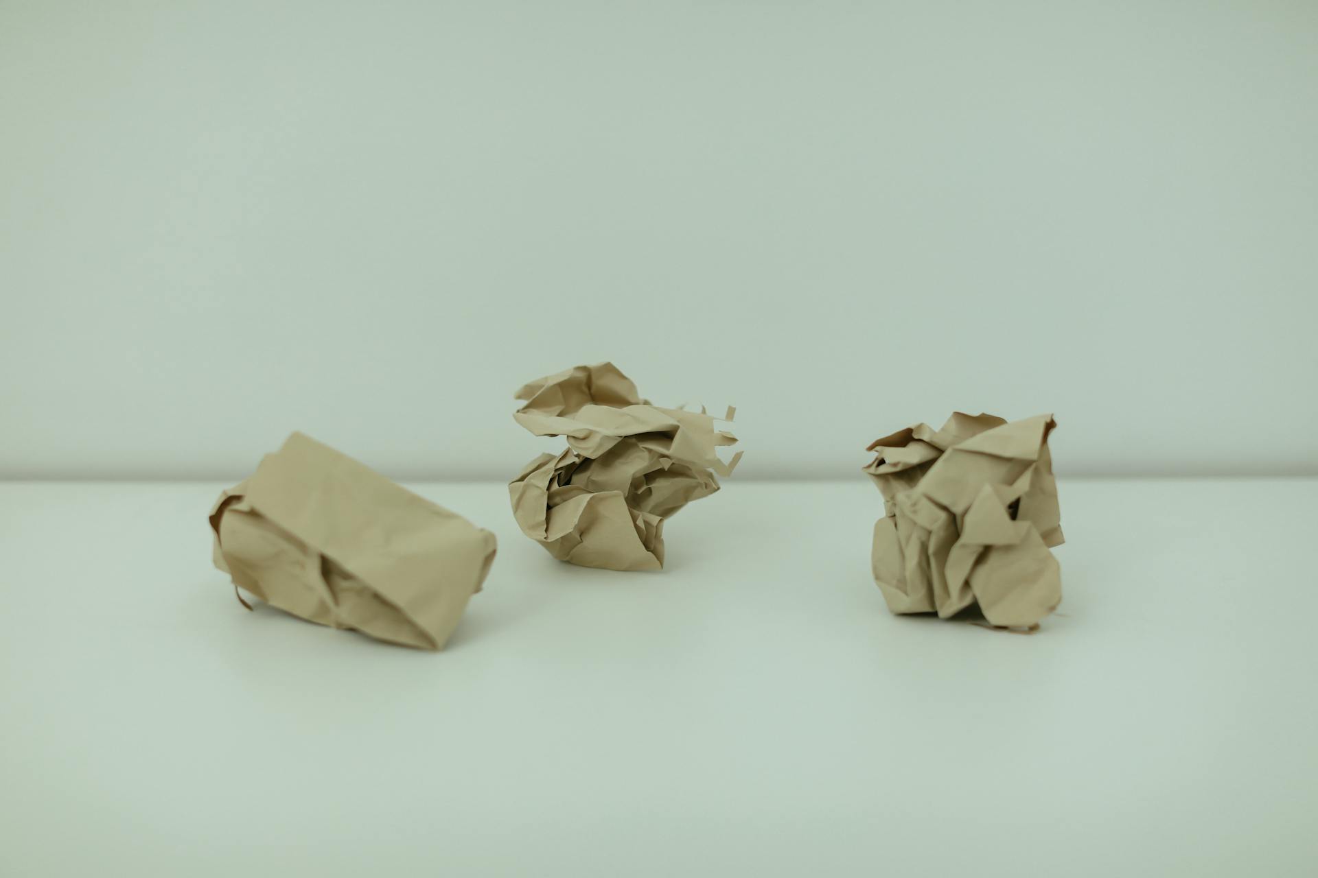3 papeles arrugados encima de una mesa del mismo color que la pared
